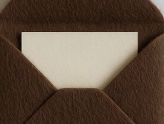 A close-up of a brown felt envelope with a blank cream-colored card partially tucked inside.