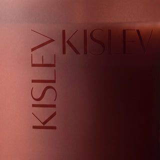 Close-up of a chestnut brown candle with the brand name KISLEV printed vertically and horizontally in a matching dark tone.