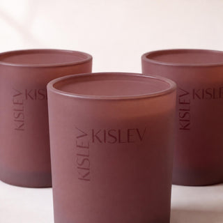 Three matte glass candle jars in a chestnut brown color, arranged in a row. The front jar is in sharp focus, displaying the embossed brand name 'KISLEV', while the rear jars are softly blurred.
