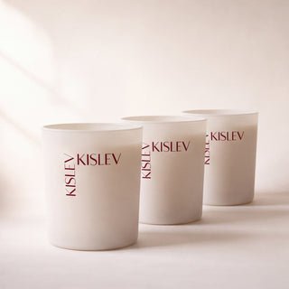 Three matte linen glass candles with the brand name 'KISLEV' printed vertically in dark brown, arranged in a row on a light beige background.