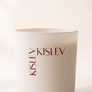 A matte linen glass candle jar with the brand name 'KISLEV' printed in dark brown on the front, set against a soft, warm off-white background.