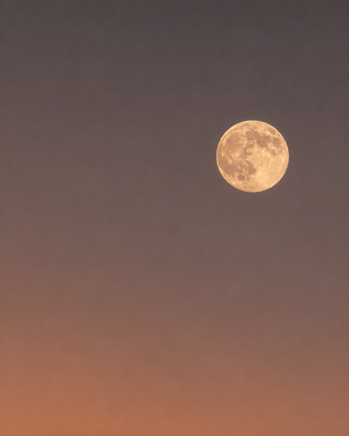 A full moon glowing with a warm golden-orange hue against a dark gray sky with a soft orange glow near the bottom.