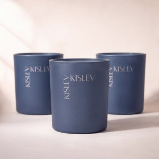 Three matte blue cylindrical candle jars with the brand name 'KISLEV' printed vertically, arranged in a studio setting with soft shadows.