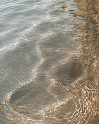 Close-up of rippling shallow water over a sandy surface, with light reflecting across the clear water and warm tan sand visible.